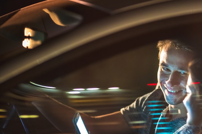 El hombre y la mujer felices sentados en el coche y el móvil. Noche de la tarde