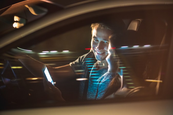 El hombre y la mujer felices sentados en el coche y el móvil. Noche de la tarde