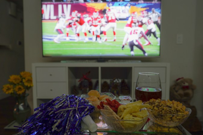 Tiempo del juego Super Bowl en casa con aperitivos y cerveza y Pom-Pom, fondo no enfocado con pantalla de TV