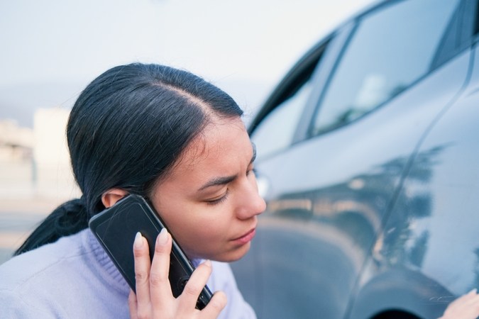 Mujer llamando al seguro de auto examinando los daños en el auto