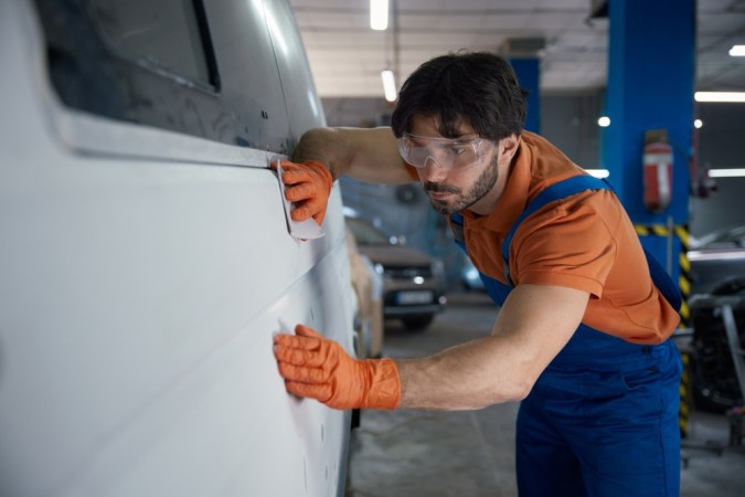 Un técnico de carrocería está inspeccionando meticulosamente un panel de automóvil en el taller de reparación hoy