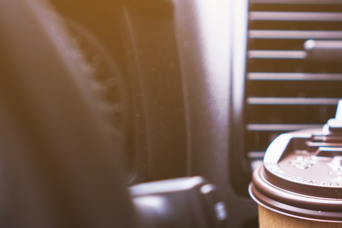 Portavasos sosteniendo una taza de café de papel mientras conduce un auto por la mañana.