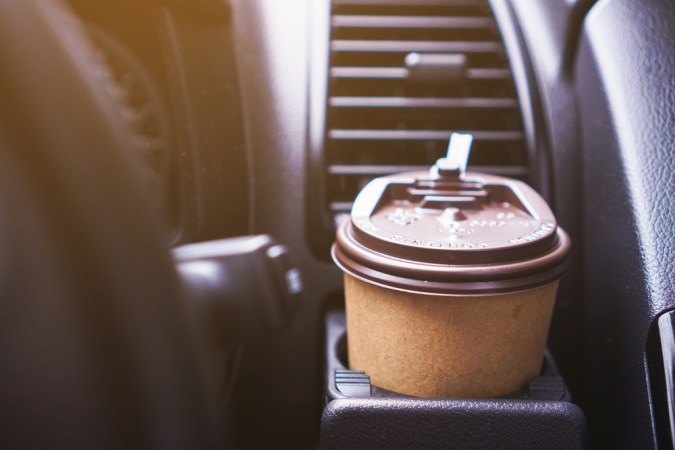 Portavasos sosteniendo una taza de café de papel mientras conduce un auto por la mañana.