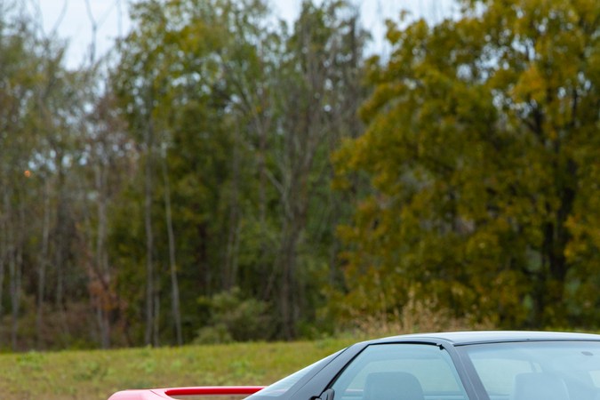 Perfil lateral del Acura NSX clásico rojo 1991 estacionado, puertas alas de murciélago y chasis de aluminio ligero