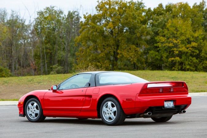 Vista trasera del Acura NSX clásico rojo de 1991 en carretera, destacando diseño aerodinámico y llantas deportivas.