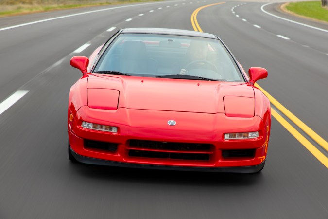 Acura NSX 1991 rojo acelerando en carretera, perfil frontal con motor central y líneas agresivas del superdeportivo japonés.