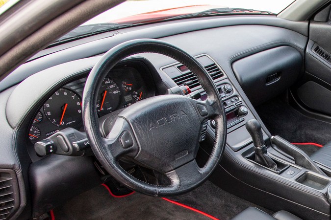 Interior del Acura NSX clásico 1991, volante, asientos deportivos en cuero negro y paneles rojos en cabina compacta.