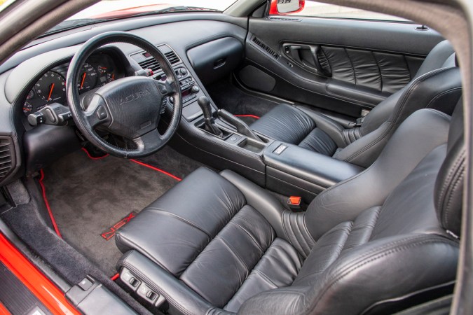 Interior del Acura NSX clásico 1991, volante, asientos deportivos en cuero negro y paneles rojos en cabina compacta.