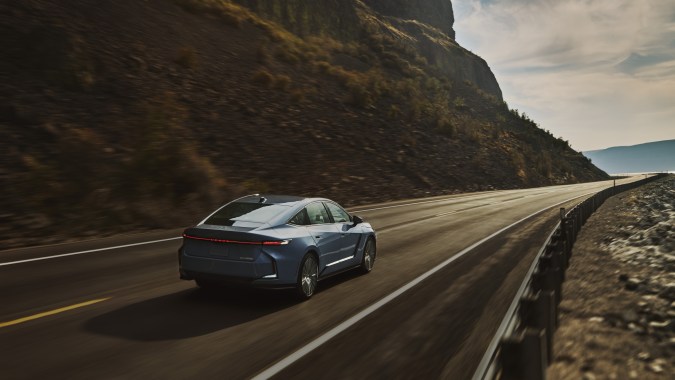 Lexus ES500e 2026 EV en carretera montañosa, sedán eléctrico de lujo con diseño aerodinámico.