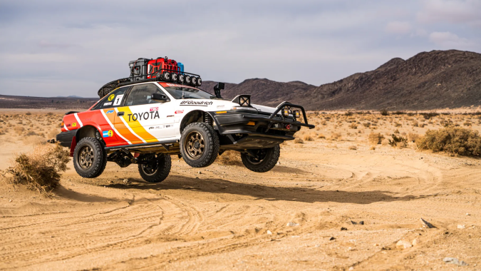 Toyota Corolla AWDROLA en rally safari off-road, levantando arena en desierto extremo.