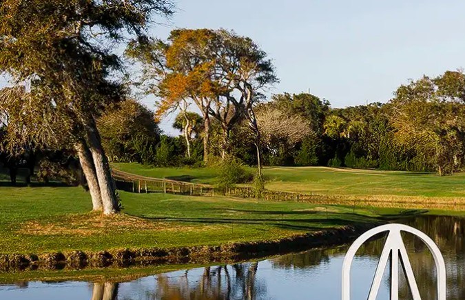 Escena del Amelia Concours d’Elegance 2026 con autos clásicos junto al lago, césped del campo de golf y gran escultura del logo del evento