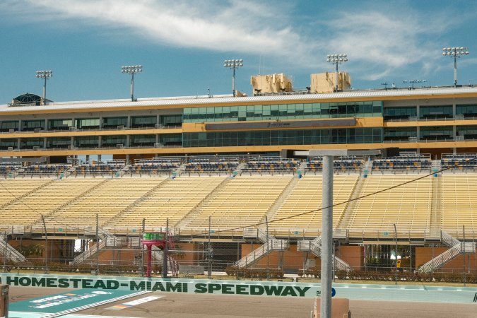Carreras legales de autos en pista ovalada Homestead-Miami Speedway, con vehículos en curva bajo graderías amarillas. Evento automovilístico Florida 2026