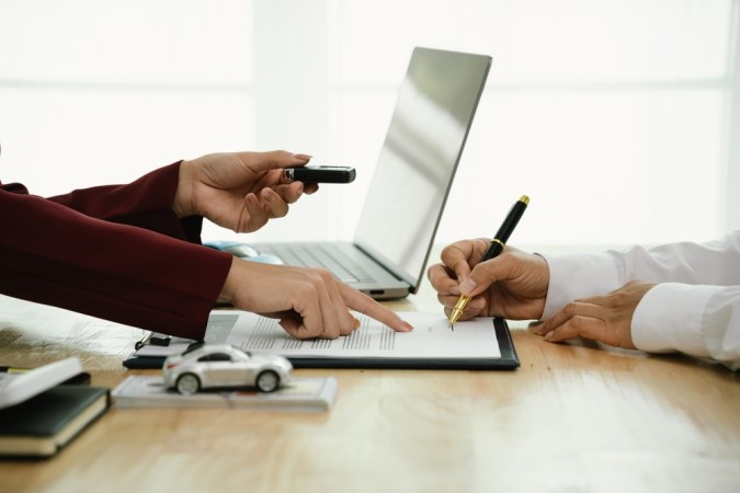 Un hombre de negocios y un cliente completan un Acuerdo firmando documentos para el seguro de automóvil, préstamo o alquiler, simbolizando finanzas, contratos, pólizas, inversiones, compras, trámites legales y propiedad segura