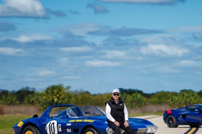 Corvette Grand Sport clásico azul y Corvette C8 moderno en pista, comparativa generaciones, autos deportivos Chevrolet, cielo despejado, enfoque en diseño y herencia de competición.