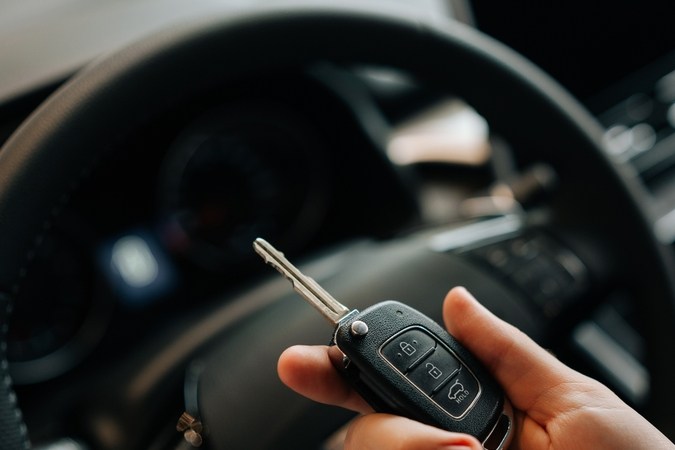 Primer plano recortado tiro de conductor irreconocible masculino que sostiene la llave de un coche nuevo en la mano. Vista de cerca de hombre feliz sentado en el asiento del conductor detrás del volante en el coche. Concepto de tecnología de coche llave inteligente.
