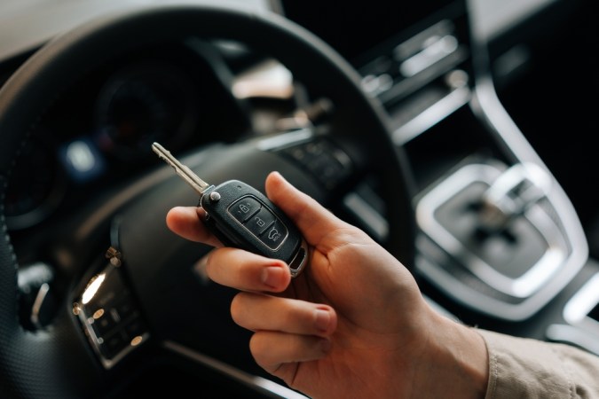 Primer plano recortado tiro de conductor irreconocible masculino que sostiene la llave de un coche nuevo en la mano. Vista de cerca de hombre feliz sentado en el asiento del conductor detrás del volante en el coche. Concepto de tecnología de coche llave inteligente.