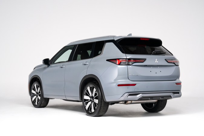 Vista trasera tres cuartos del Mitsubishi Outlander 2026 gris, SUV híbrido enchufable con rines grandes y diseño aerodinámico para ciudad y carretera