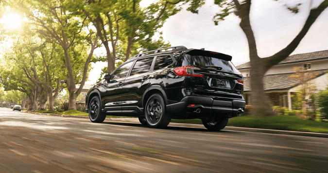 Subaru Ascent 2026 negro en movimiento por calle residencial arbolada, vista trasera lateral con efecto de velocidad