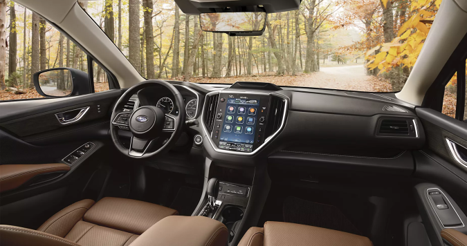 Interior del Subaru Ascent 2026 con asientos en cuero marrón, pantalla táctil y vista panorámica a bosque otoñal