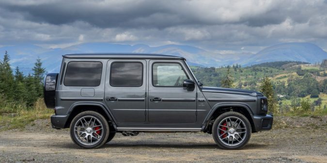 Vista lateral del icónico SUV de lujo Mercedes G-Wagon en paisaje montañoso con ruedas de alto rendimiento.