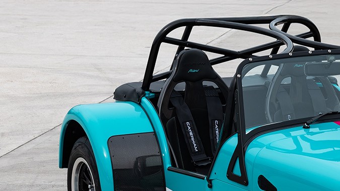 Frente del Caterham Seven Miami Edition con carrocería turquesa, franjas rosas y diseño retro deportivo inspirado en la Fórmula 1.
