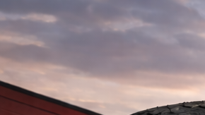 Primer plano de neumático Firestone frente a taller automotriz al atardecer, con camioneta y SUV sobre asfalto mojado iluminado por luz cálida.
