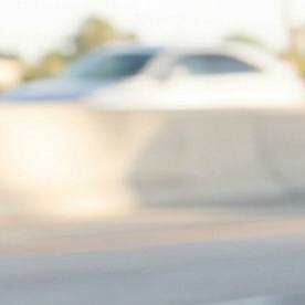 Vista en primer plano de un espejo retrovisor reflejando un SUV que sigue muy de cerca a un sedán en la carretera, con un primer plano de un volante.