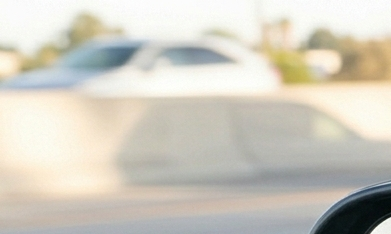 Vista en primer plano de un espejo retrovisor reflejando un SUV que sigue muy de cerca a un sedán en la carretera, con un primer plano de un volante.