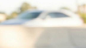 Vista en primer plano de un espejo retrovisor reflejando un SUV que sigue muy de cerca a un sedán en la carretera, con un primer plano de un volante.