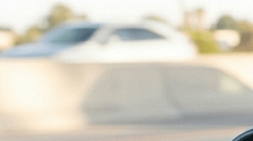 Vista en primer plano de un espejo retrovisor reflejando un SUV que sigue muy de cerca a un sedán en la carretera, con un primer plano de un volante.