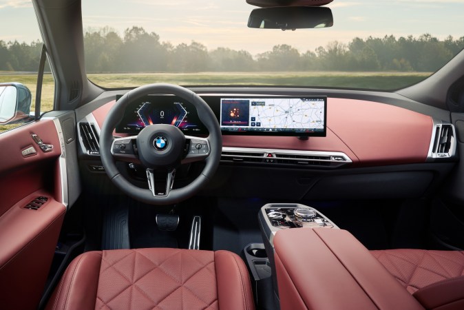 Interior de lujo del BMW iX: salpicadero y asientos en cuero rojo con pantalla curva y volante deportivo.