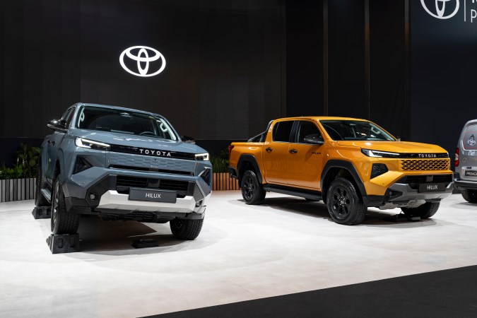 Dos pick-ups Toyota Hilux, una en gris y otra en amarillo, expuestas en el stand de Toyota del Brussels Motor Show 2026 con iluminación moderna.