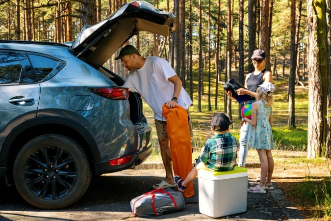 familia con niños retire los suministros de camping del maletero del coche en el bosque. vacaciones de verano, viaje por carretera