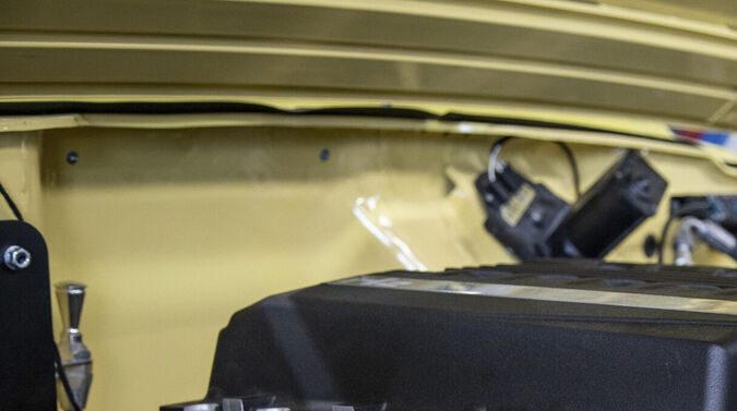 Detalle de motor de combustión en vano motor amarillo con manos de mecánico: close-up de bloque motor y componentes mecánicos durante mantenimiento automotriz.