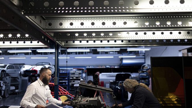 Ingenieros revisando motor en taller de desarrollo automotriz: equipo técnico trabajando en prototipo de vehículo en fábrica especializada.
