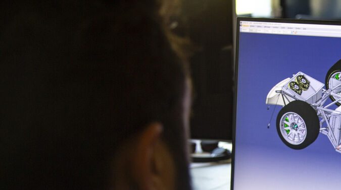 Ingeniero analizando diseño 3D de chasis y motor de vehículo en computadora: vista trasera de profesional trabajando en software de ingeniería automotriz.