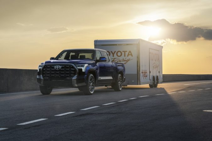Toyota Tundra 2024 Platinum azul remolcando tráiler Toyota Racing al atardecer, demostrando capacidad de remolque, estabilidad y desempeño para trabajo y aventura.