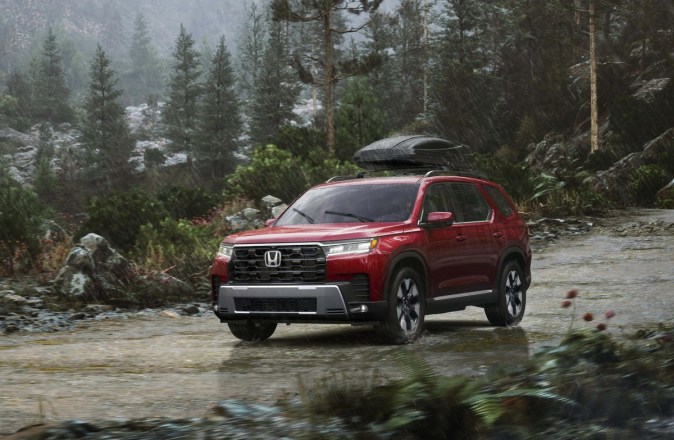 Honda Pilot Elite 2026 roja en camino off-road bajo la lluvia con roof box
