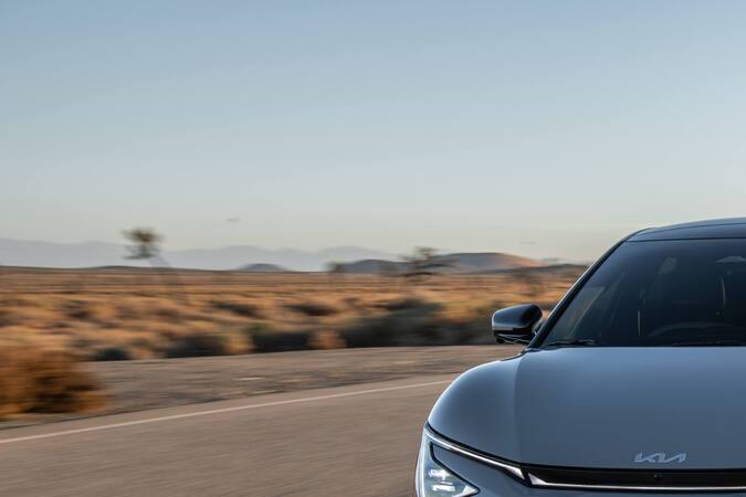 Kia EV6 2026 plateado manejando en carretera curva desértica al atardecer