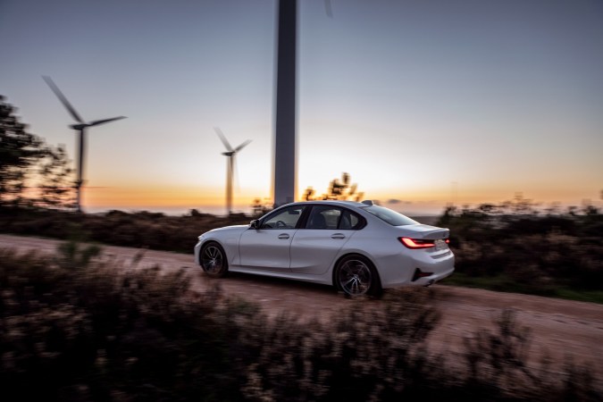BMW 330e Sedán híbrido enchufable circulando al atardecer junto a turbinas eólicas, mostrando movilidad electrificada y eficiencia en carretera rural.