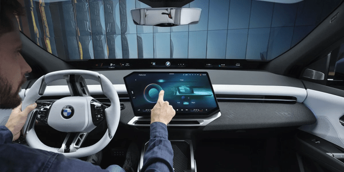Interior BMW iX3 50: conductor usando la gran pantalla táctil en el moderno cockpit del SUV eléctrico premium.