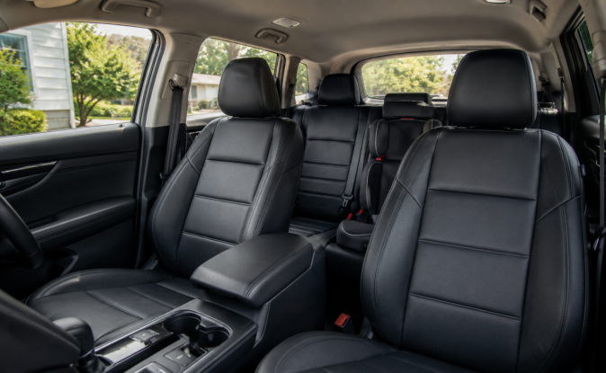 Interior de SUV con asientos de cuero negros y una silla infantil instalada en la segunda fila, mostrando configuración de asientos y seguridad para niños.