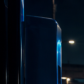 Auto eléctrico cargándose de noche con cable de luz azul e impuestos al fondo