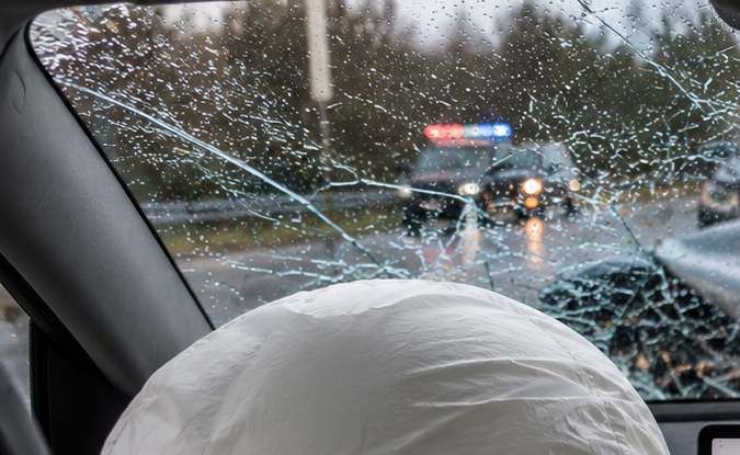 Interior Tesla tras accidente con airbags desplegados y parabrisas destrozado en día lluvioso