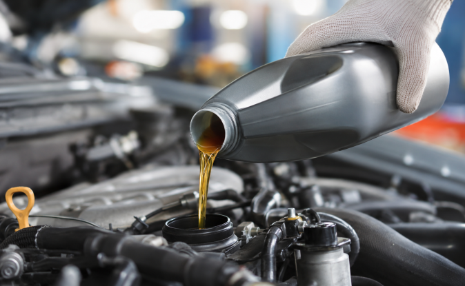 Cambio de aceite sintético en motor de auto con frasco genérico y mano con guante en taller mecánico.