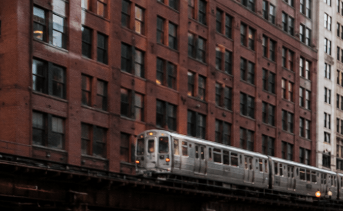 Parquímetro moderno en calle del centro de Chicago, autos estacionados junto a vía elevada del tren y rascacielos de fondo.