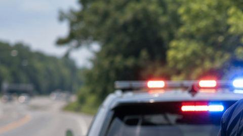 Policía de tránsito toca puerta de auto gris detenido, patrulla con luces encendidas al fondo, inspección de tráfico en carretera rural en Estados Unidos.