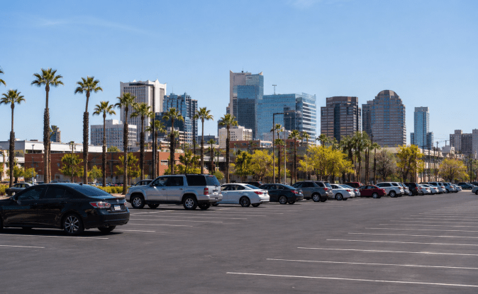 Amplio lote de estacionamiento al aire libre en ciudad de Estados Unidos, filas de autos aparcados con palmeras y rascacielos al fondo