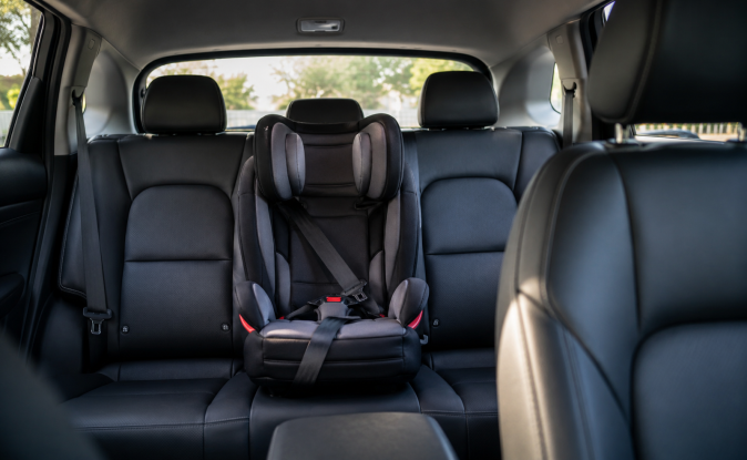 Silla infantil negra instalada en asiento trasero central de auto, destacando posición segura para niños con cinturón de seguridad ajustado.