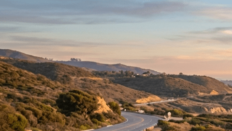 “Tesla Model 3 azul y Tesla Model Y rojo circulando por carretera costera al atardecer, autos eléctricos en carretera panorámica junto al mar en 2026
